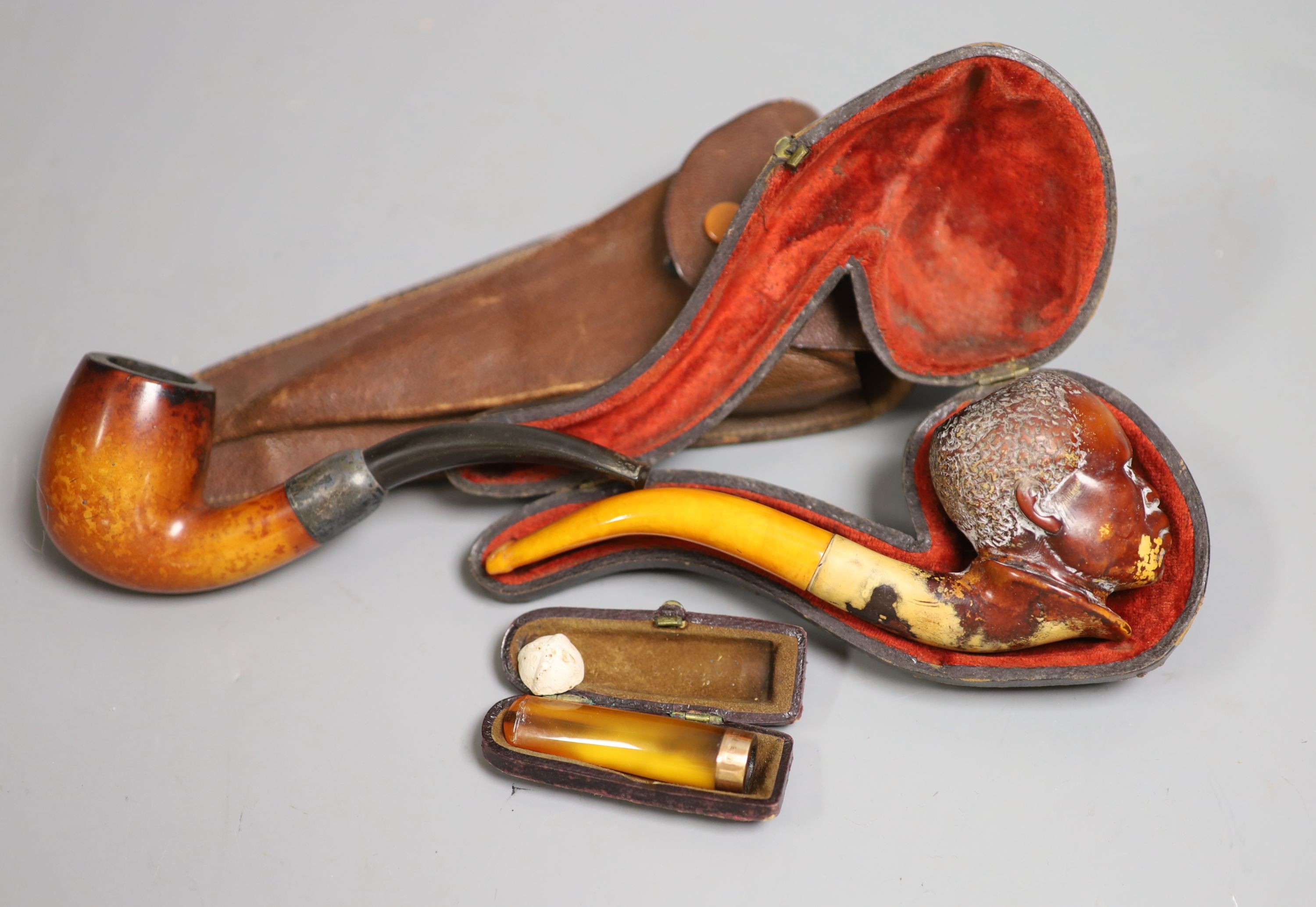 A Meerschaum and amber carved head (cased), 14.5cm long, an amber and gold cigarette holder and a wooden pipe